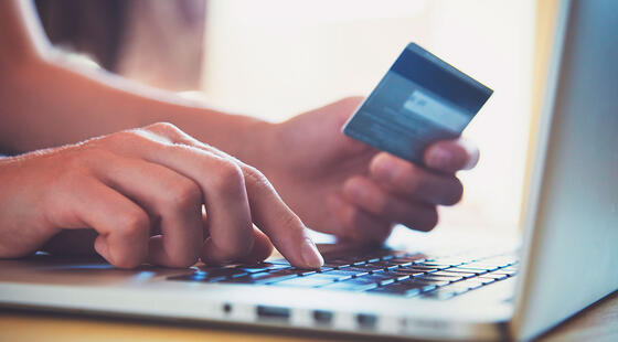 Manos sujetando una tarjeta de crédito enfrente de un ordenador portátil