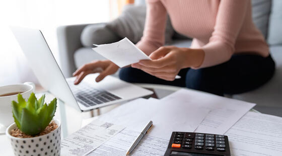 Mujer sentada enfrente de un ordenador portátil mientras sujeta un papel con una mano y teclea con la otra