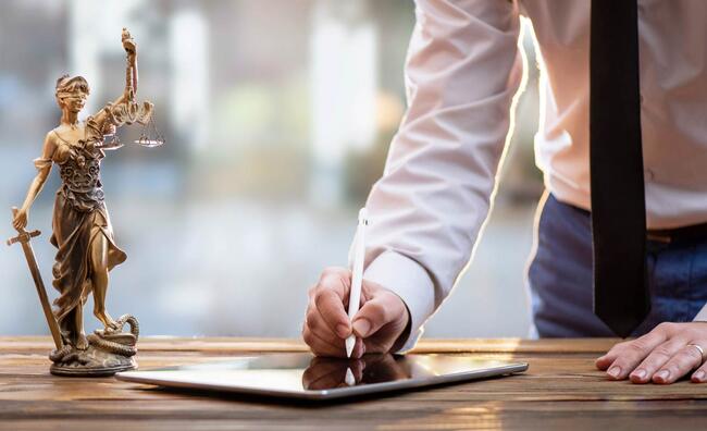 Persona firmando en un iPad al lado de una estatua de Themis