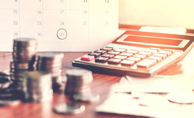 Calendario, calculadora y monedas sobre una mesa de madera